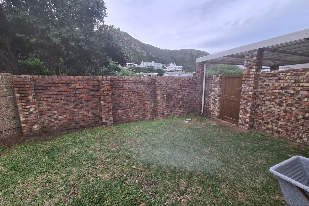 A private rear garden area featuring a face brick boundary wall, a small lawn, and a covered patio structure with a timber access gate.