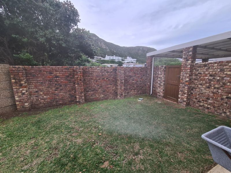 A private rear garden area featuring a face brick boundary wall, a small lawn, and a covered patio structure with a timber access gate.