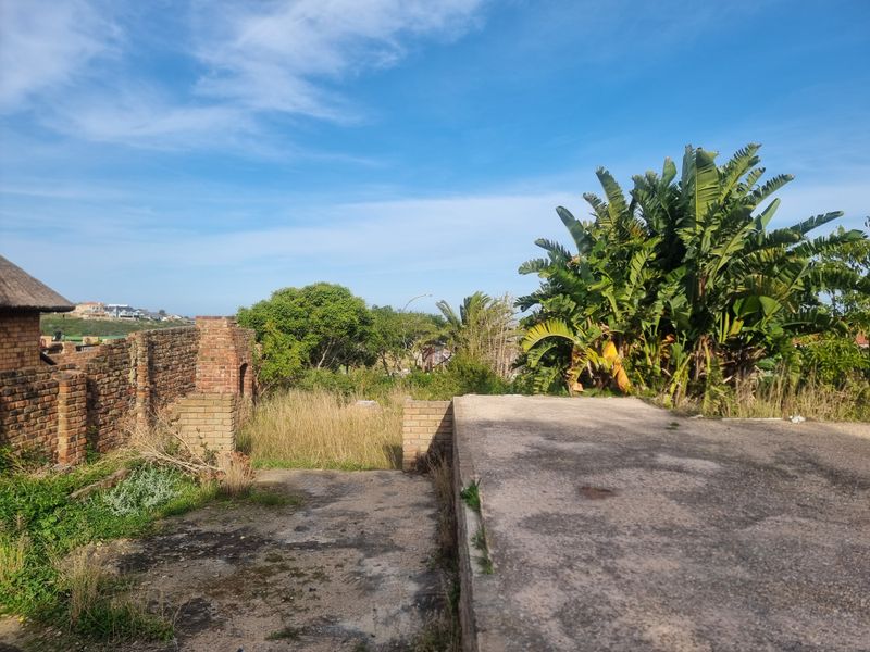 A view of a vacant residential plot featuring a concrete slab foundation, brick boundary walls, and established garden vegetation.