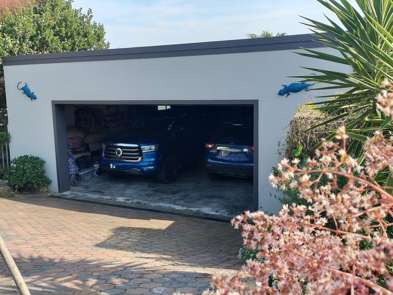 A detached double garage featuring a paved driveway and a modern flat roof design, situated in a landscaped garden setting.