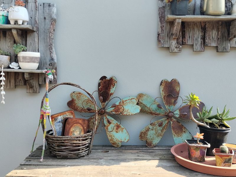 A close-up view of decorative wall-mounted wooden shelving and metal garden ornaments against a plain exterior wall.