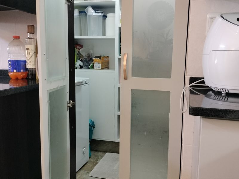 A functional scullery or pantry area featuring built-in shelving, granite countertops, and a modern frosted glass door for organized storage.