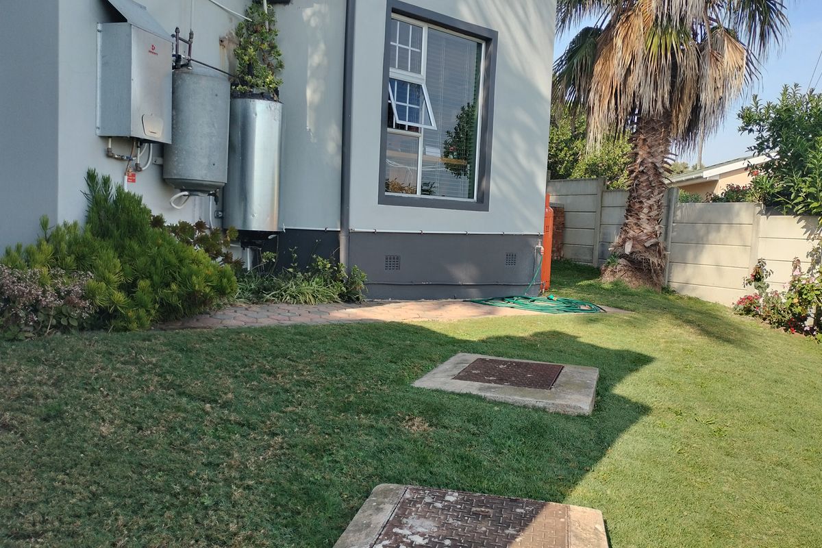 Rear exterior view showing a lawn area, paved path, gas geyser installation, and water storage tank against the building facade.