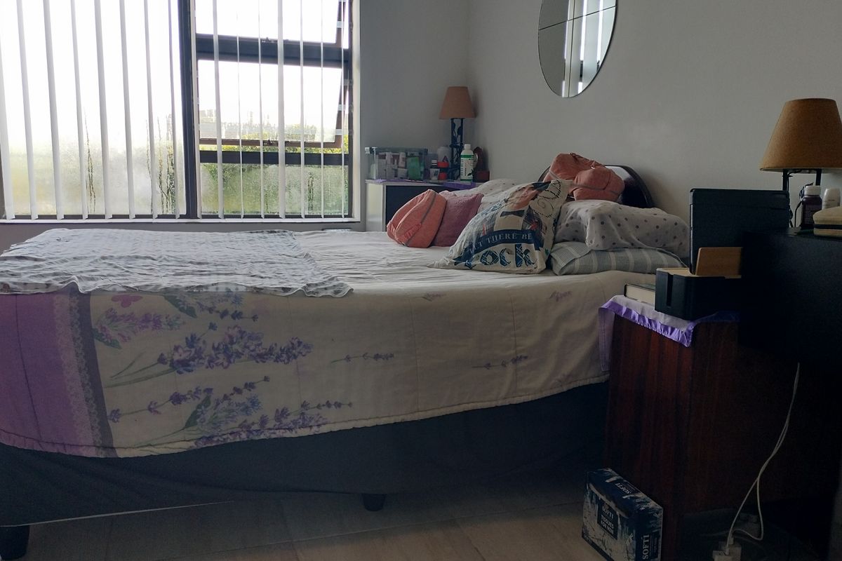 A functional bedroom featuring tiled flooring, large aluminium-framed windows with vertical blinds, and neutral wall finishes.