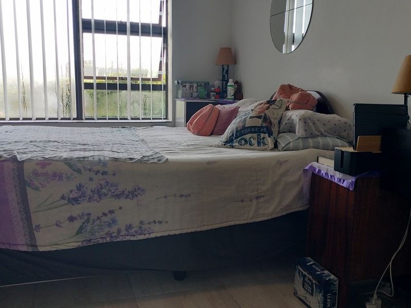 A functional bedroom featuring tiled flooring, large aluminium-framed windows with vertical blinds, and neutral wall finishes.