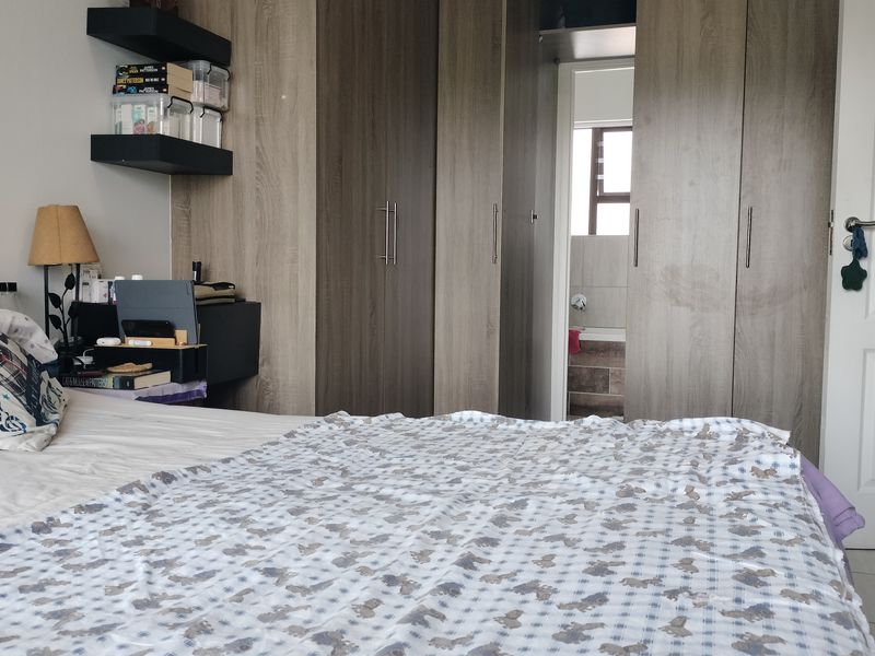 A bedroom featuring modern wood-finish built-in cupboards, floating shelving, and direct access to an en-suite bathroom.
