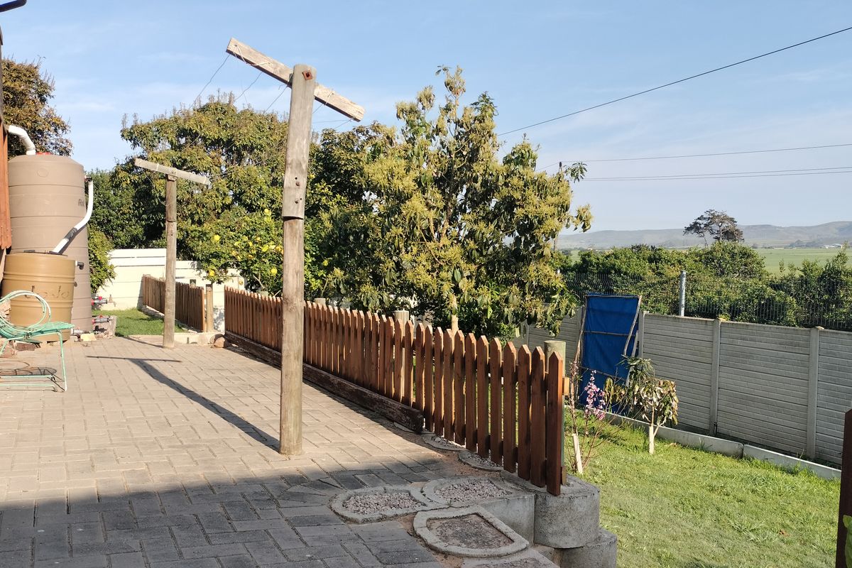 A rear outdoor area featuring a paved patio, wooden picket fencing, and a water storage tank, overlooking a garden with distant landscape views.