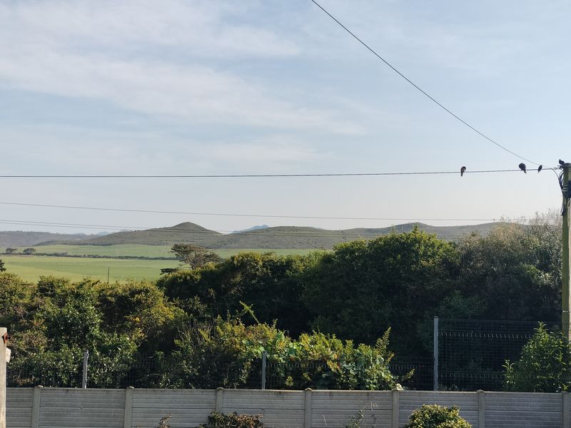 A scenic view overlooking rolling green hills and natural landscape, framed by a boundary wall and utility infrastructure.