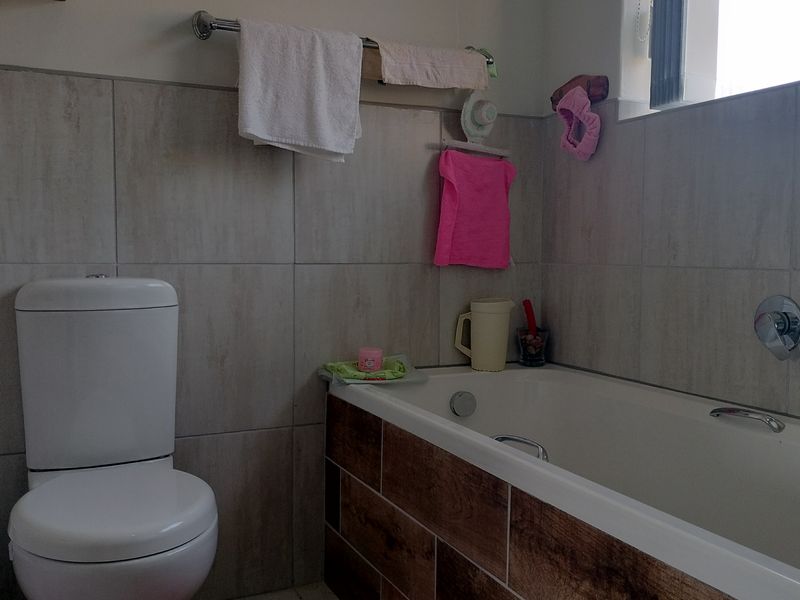 A functional bathroom featuring a bathtub with wall-mounted mixer tap, a standard toilet, and neutral wall tiling.