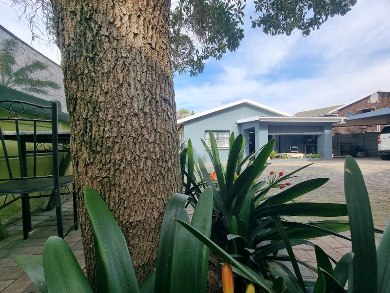 Front view of the property featuring a paved driveway, covered entrance area, and established garden surroundings.