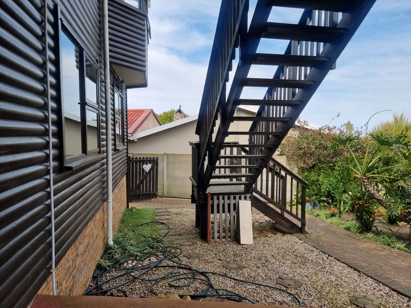 Rear exterior view featuring an external timber staircase, paved garden path, and timber-clad building facade.