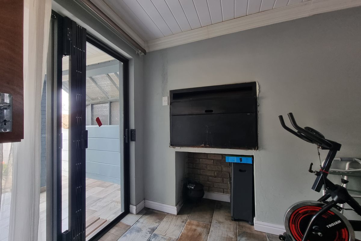 Living area featuring a built-in braai, tongue and groove ceiling, and stacking doors providing direct access to the outdoor patio area.