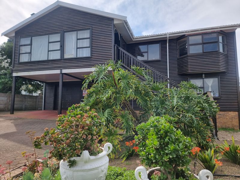 A two-story house featuring dark timber cladding, an external staircase, and a paved driveway with an integrated garage.