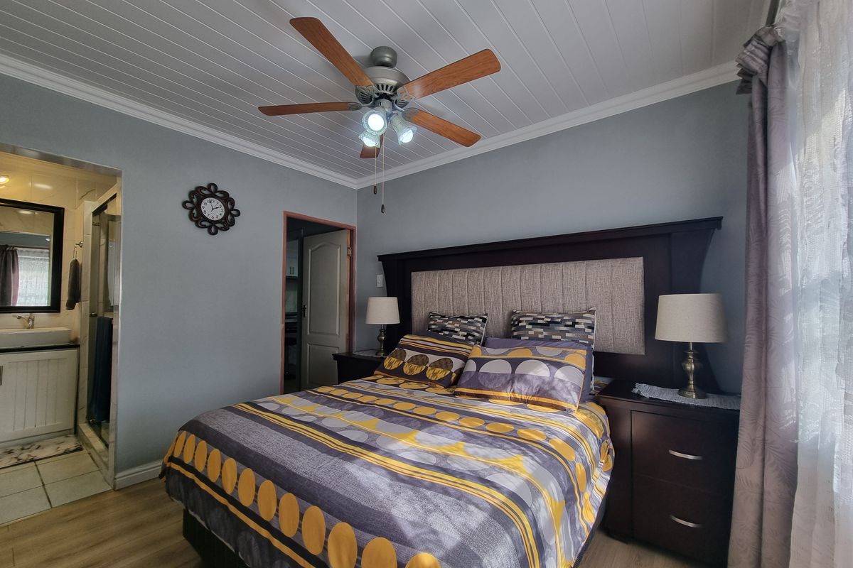 A well-maintained bedroom featuring laminate flooring, a tongue and groove ceiling with a central fan, and direct access to an en-suite bathroom.