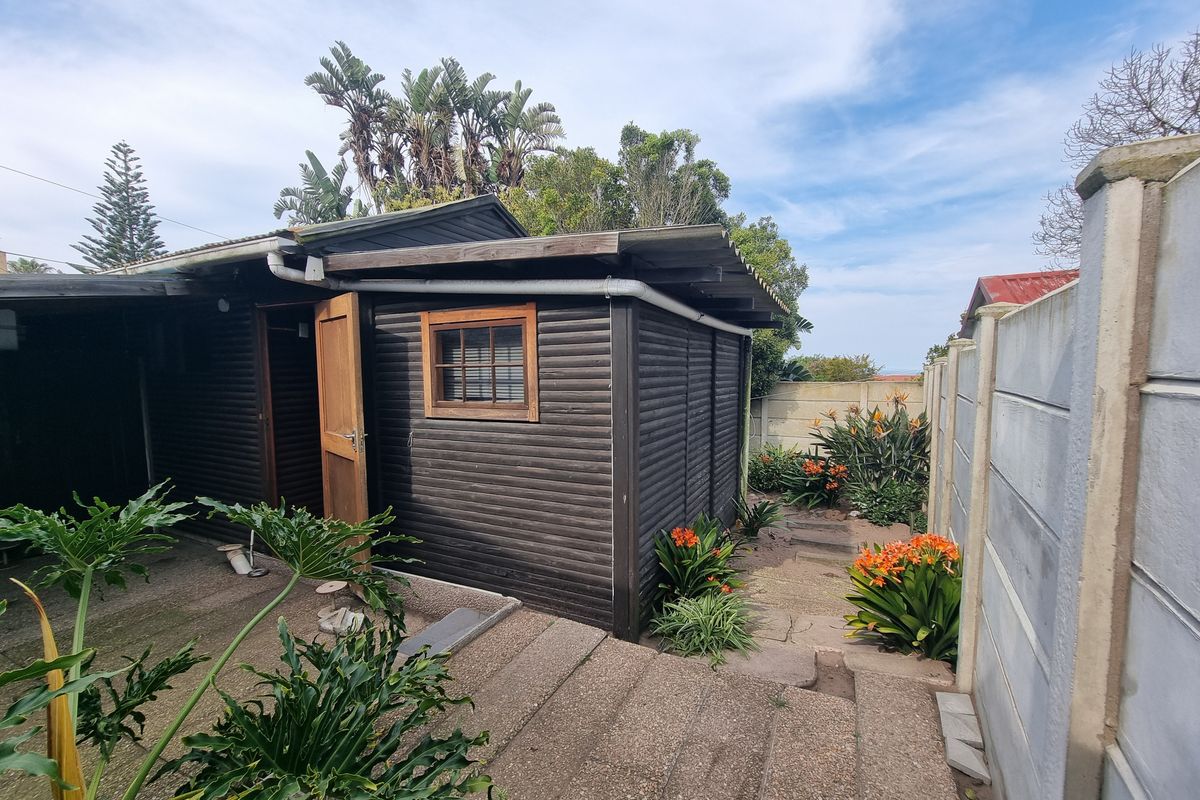 Rear exterior view of a timber-clad outbuilding featuring a paved patio area and a precast concrete boundary wall.