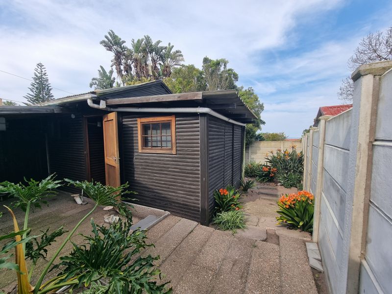 Rear exterior view of a timber-clad outbuilding featuring a paved patio area and a precast concrete boundary wall.