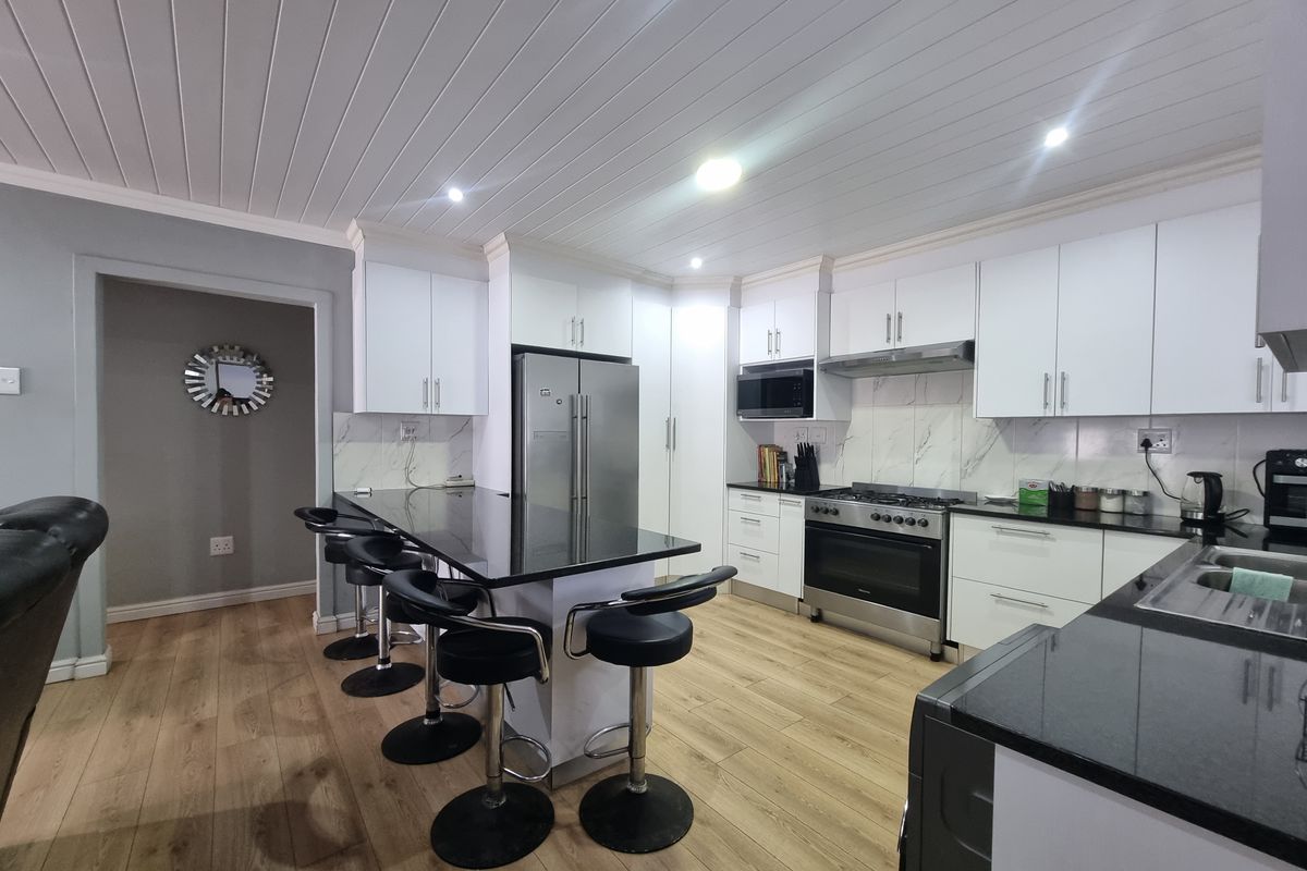 Modern kitchen featuring white cabinetry, granite countertops, a central island, and stainless steel appliances, complemented by laminate flooring and recessed lighting.