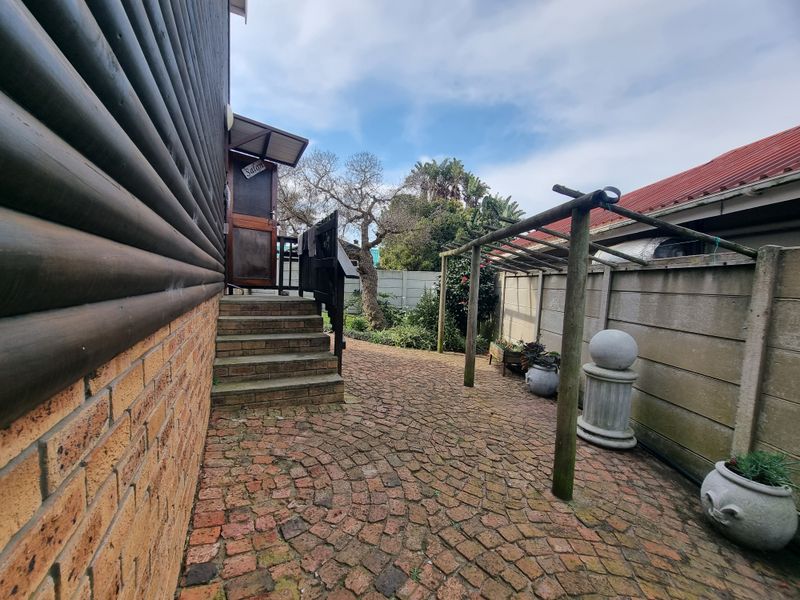 Rear exterior area featuring brick paving, a timber pergola structure, and access steps leading to the side of the log-style building.