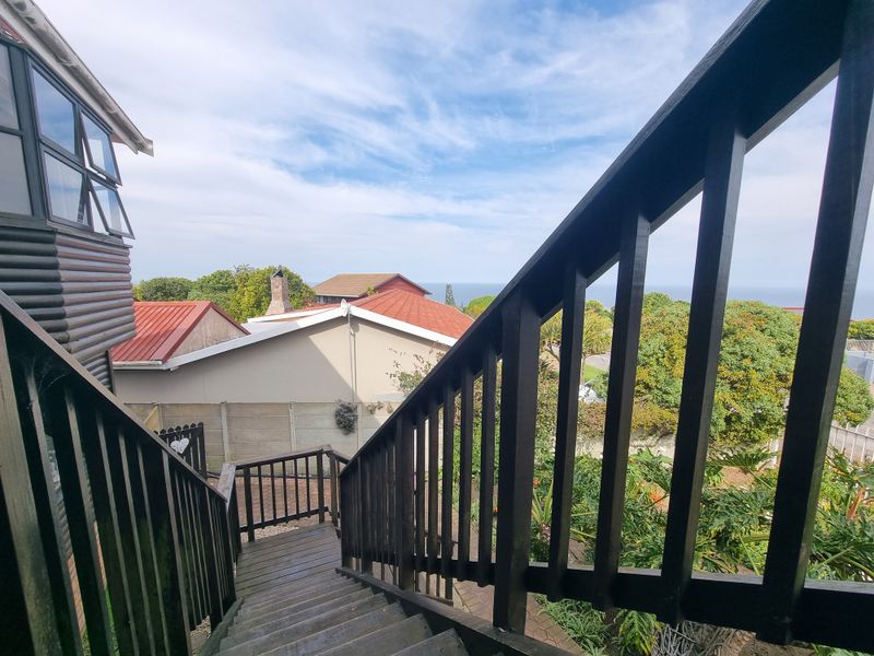 An elevated wooden staircase and balustrade leading down to the garden area, offering views of the surrounding neighborhood and distant sea.