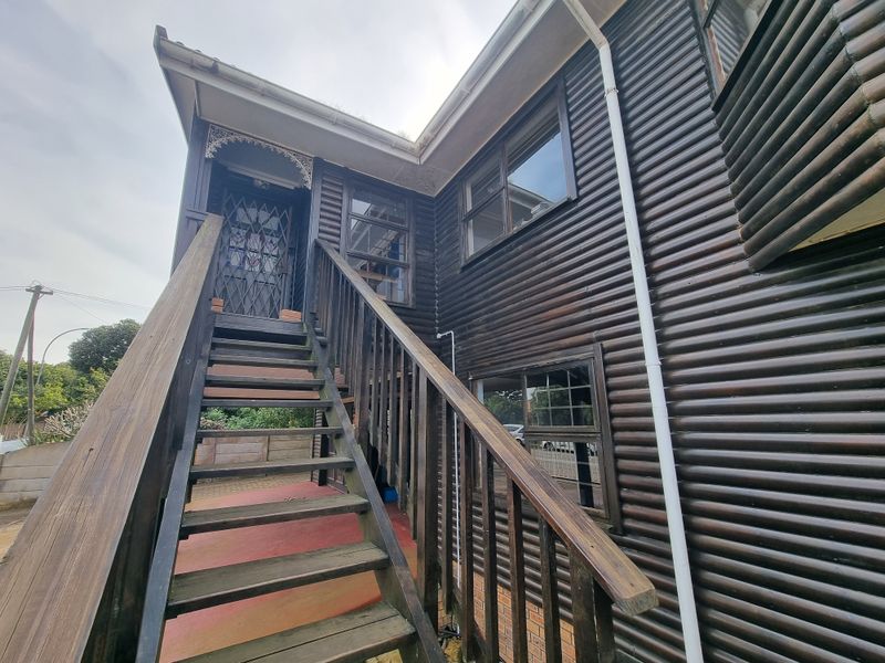 Exterior view of a timber-clad house featuring an elevated entrance accessed by a wooden staircase with a security gate.