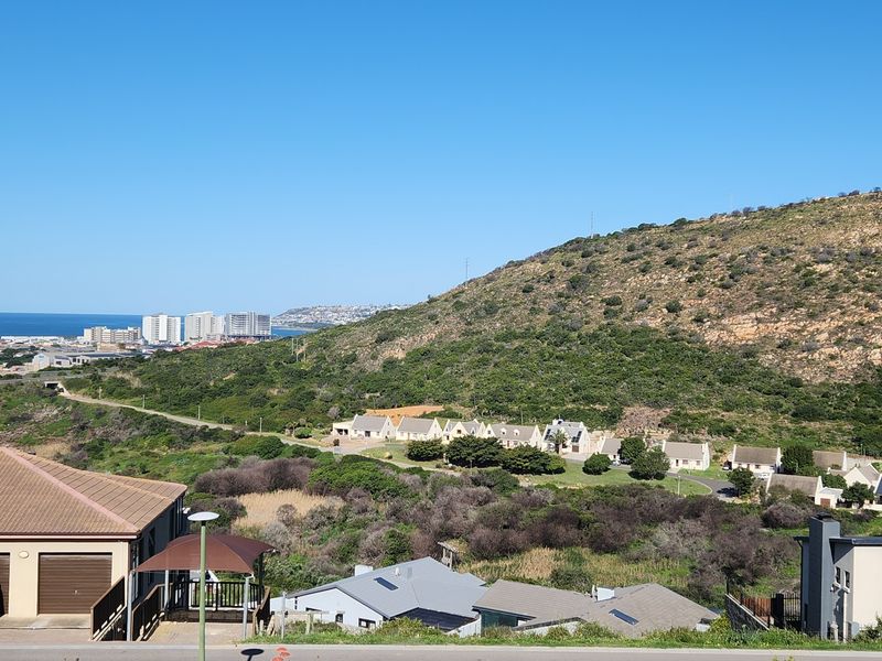A scenic elevated view overlooking a coastal landscape, hillside terrain, and surrounding residential development.