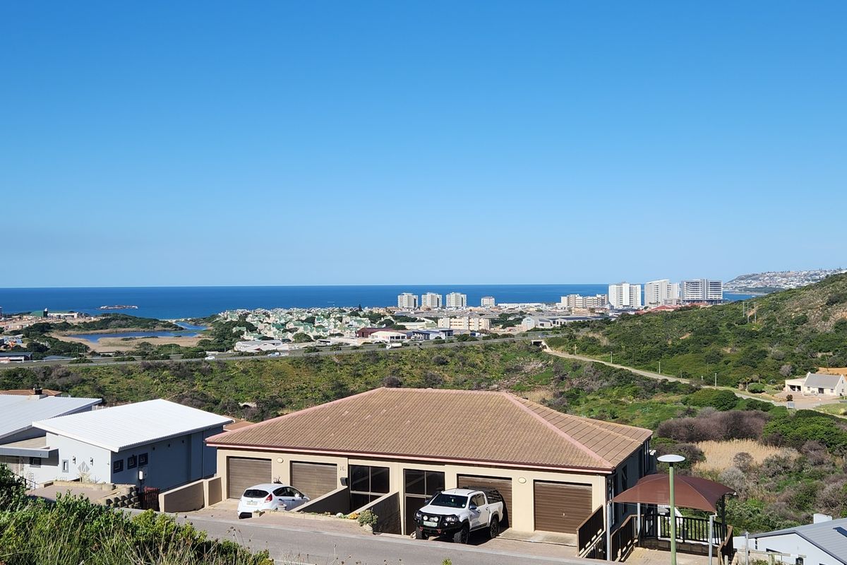 Elevated view overlooking the surrounding landscape, coastal town, and ocean horizon, featuring residential properties in the foreground.