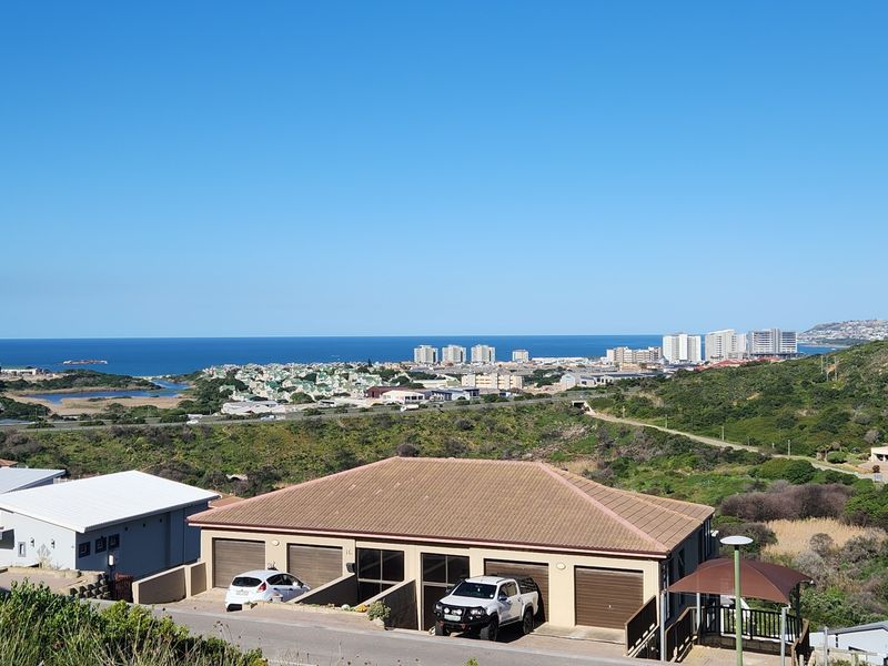 Elevated view overlooking the surrounding landscape, coastal town, and ocean horizon, featuring residential properties in the foreground.