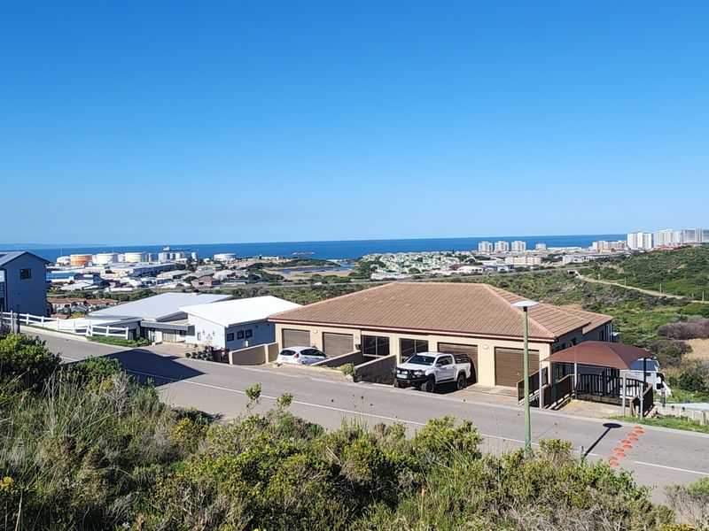 Elevated view overlooking a residential neighborhood with coastal scenery and industrial infrastructure in the distance.