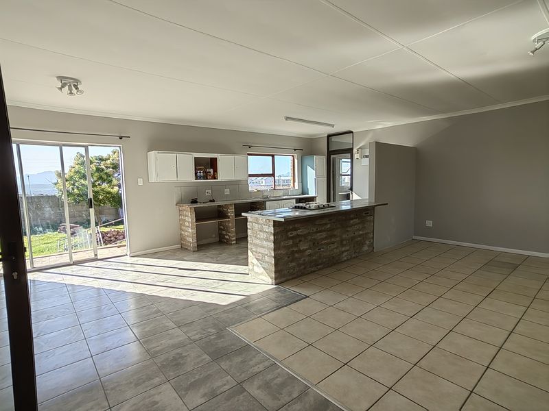 Spacious open-plan living and kitchen area featuring a brick-base island, tiled flooring, and direct access to the outdoor patio through sliding glass doors.