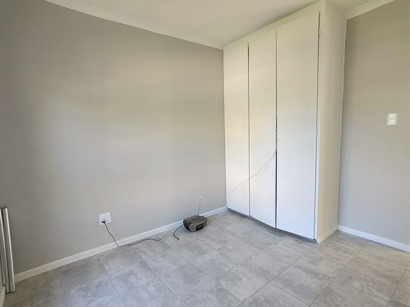 A clean, empty bedroom featuring neutral wall paint, tiled flooring, and a built-in white wardrobe.