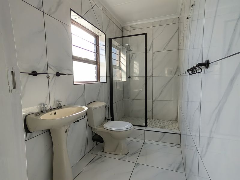 A modern bathroom featuring marble-look wall and floor tiles, a walk-in shower with a black-framed glass screen, a pedestal basin, and a toilet.