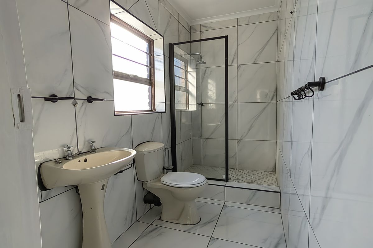 A modern bathroom featuring marble-look wall and floor tiles, a walk-in shower with a black-framed glass screen, a pedestal basin, and a toilet.