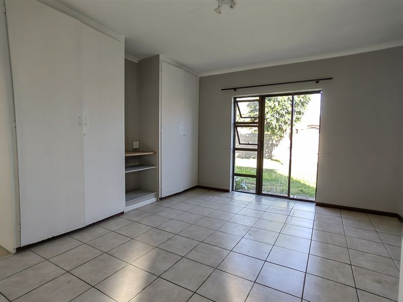 A vacant bedroom featuring tiled flooring, built-in cupboards, and a sliding glass door providing direct access to the garden.