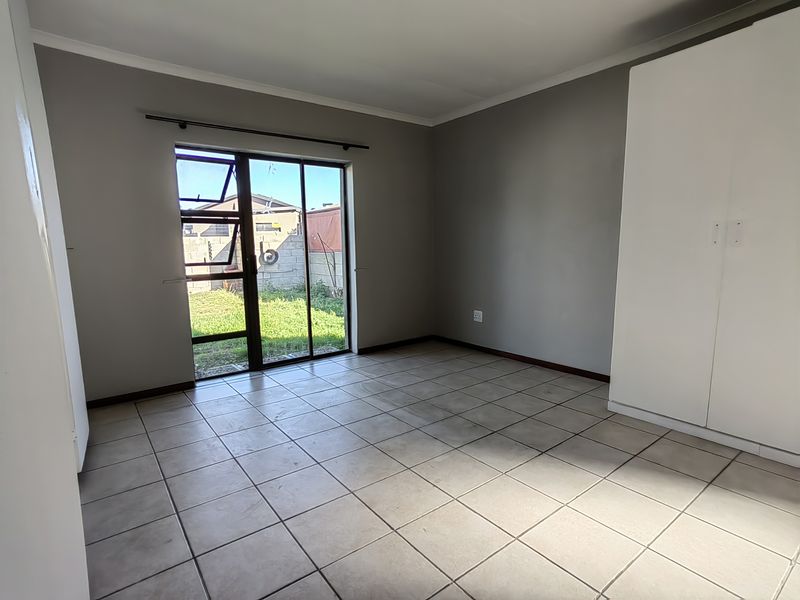 An empty bedroom featuring tiled flooring, a built-in wardrobe, and a sliding glass door providing direct access to the rear garden.