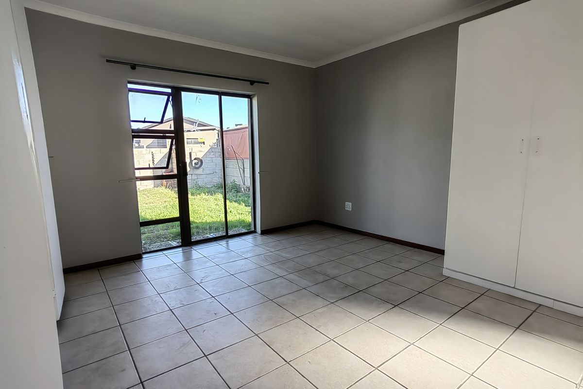 An empty bedroom featuring tiled flooring, a built-in wardrobe, and a sliding glass door providing direct access to the rear garden.