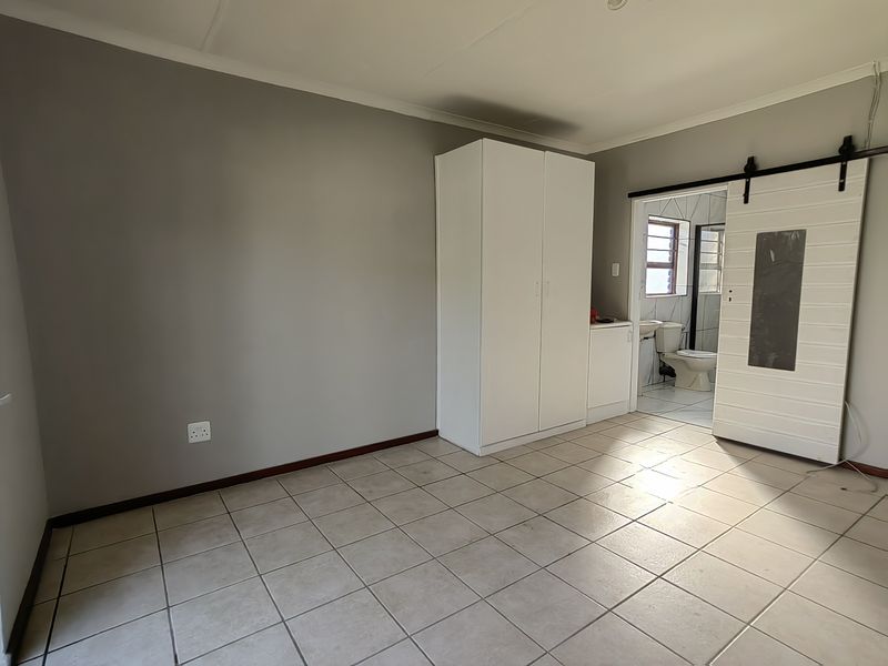 A spacious bedroom featuring tiled flooring, a built-in wardrobe, and a sliding barn door providing access to an en-suite bathroom.