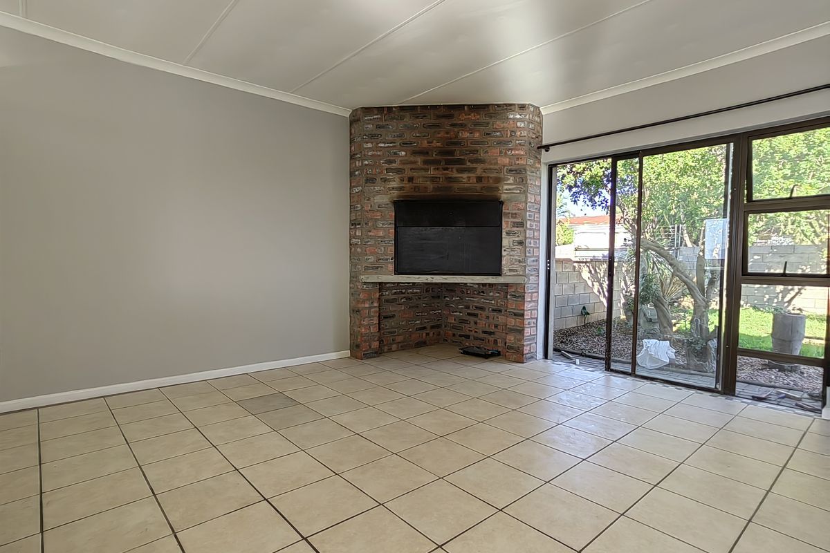 Spacious living room featuring a corner brick fireplace, neutral tiled flooring, and large sliding glass doors providing access to the rear garden.