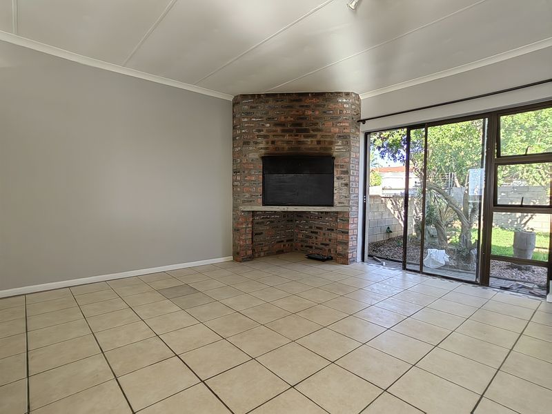 Spacious living room featuring a corner brick fireplace, neutral tiled flooring, and large sliding glass doors providing access to the rear garden.