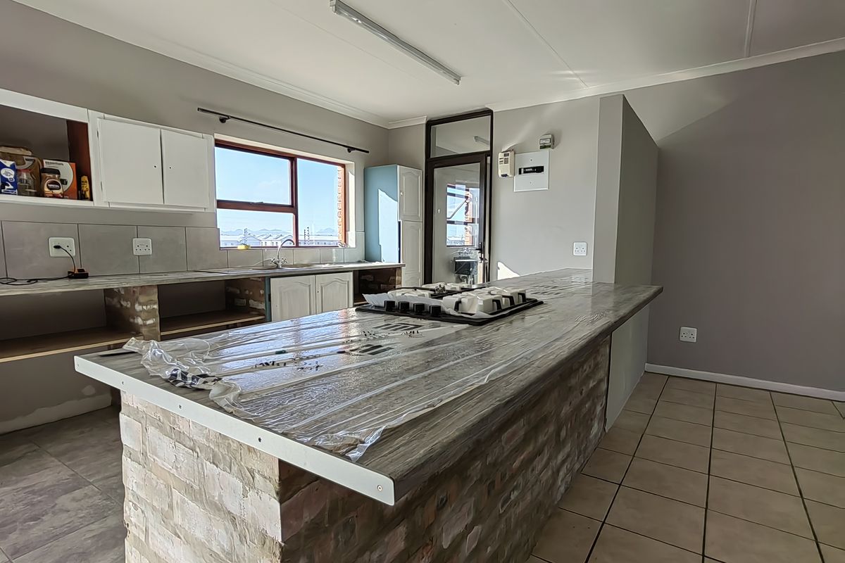 A kitchen featuring a brick island with a built-in hob, tiled flooring, and partially completed cabinetry, offering potential for custom finishing.