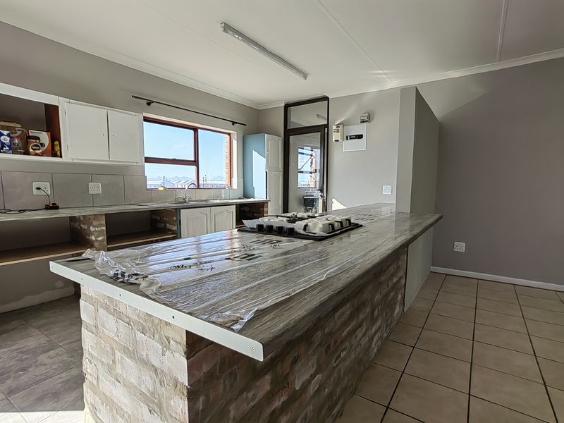 A kitchen featuring a brick island with a built-in hob, tiled flooring, and partially completed cabinetry, offering potential for custom finishing.