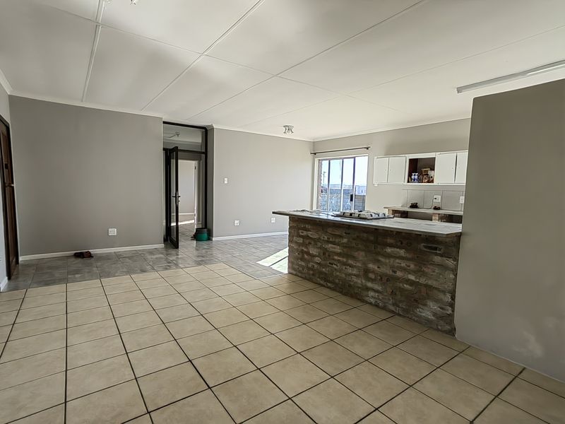 Open plan living and kitchen area featuring a brick breakfast bar, tiled flooring, and neutral wall finishes, offering a blank canvas for renovation.