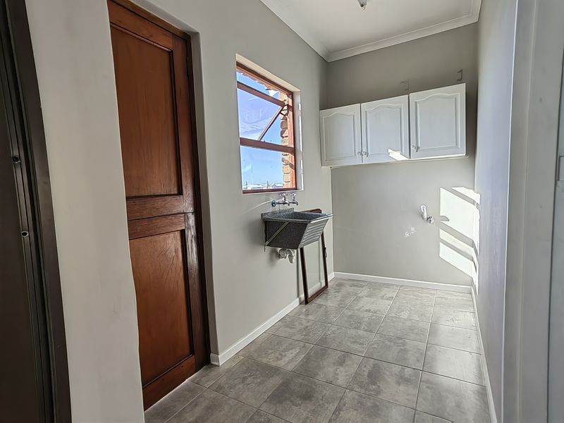 A functional laundry room featuring tiled flooring, a wall-mounted utility sink, and overhead storage cabinetry.