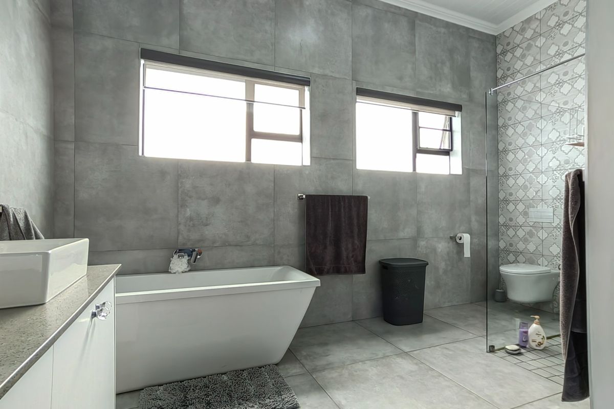 Modern bathroom featuring a freestanding bathtub, wall-mounted toilet, glass shower enclosure, and contemporary grey tiling with a decorative feature wall.