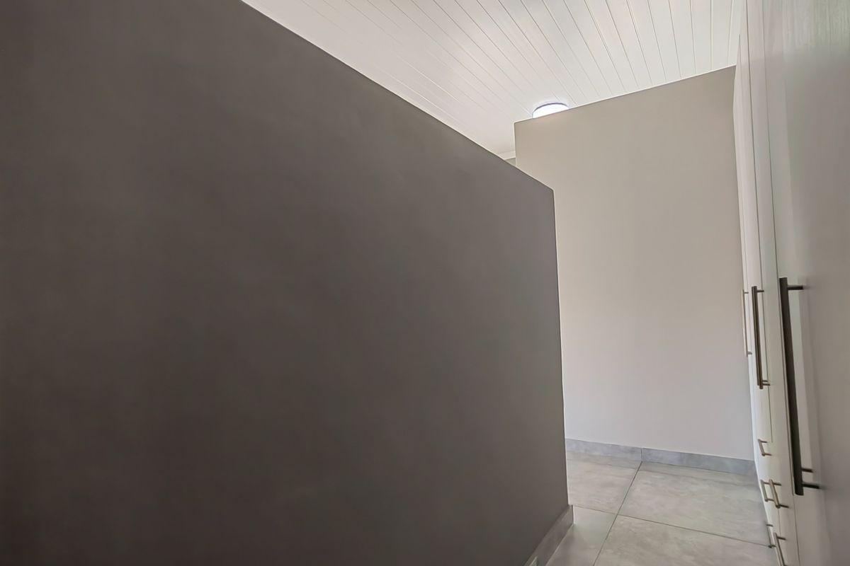 A clean, modern bedroom space featuring built-in cupboards, neutral tiled flooring, and a white tongue and groove ceiling.