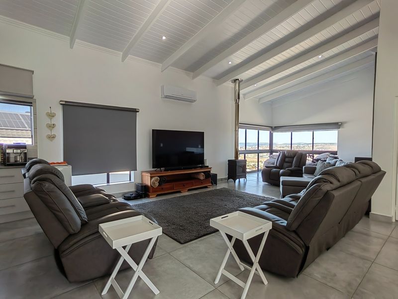 Spacious living room featuring a vaulted ceiling with exposed beams, a wood-burning fireplace, tiled flooring, and large windows offering scenic views.