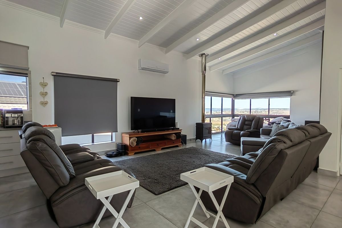 Spacious living room featuring a vaulted ceiling with exposed beams, a wood-burning fireplace, tiled flooring, and large windows offering scenic views.
