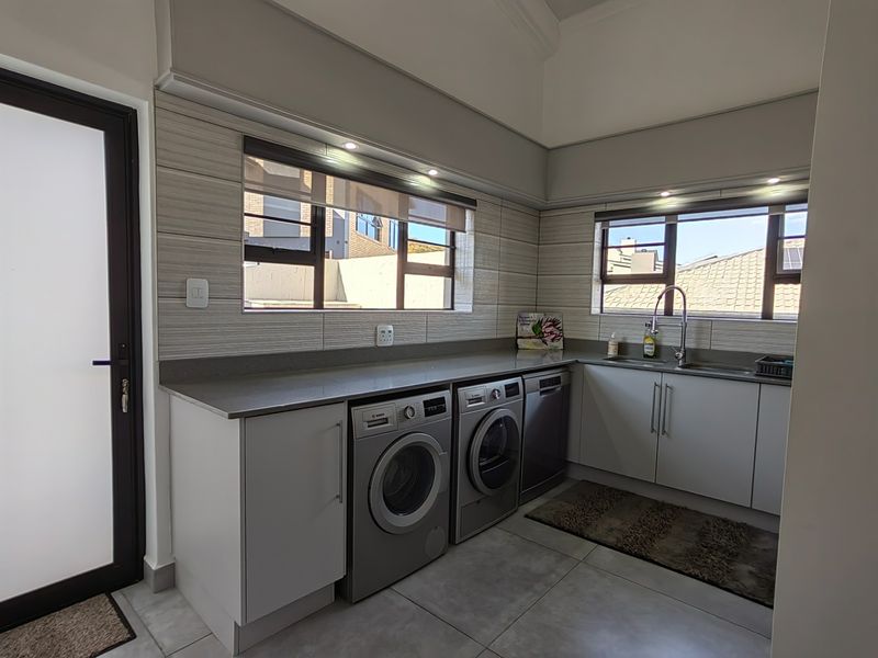 A modern, well-appointed laundry room featuring sleek built-in cabinetry, stone countertops, an undermount sink, and tiled finishes throughout.