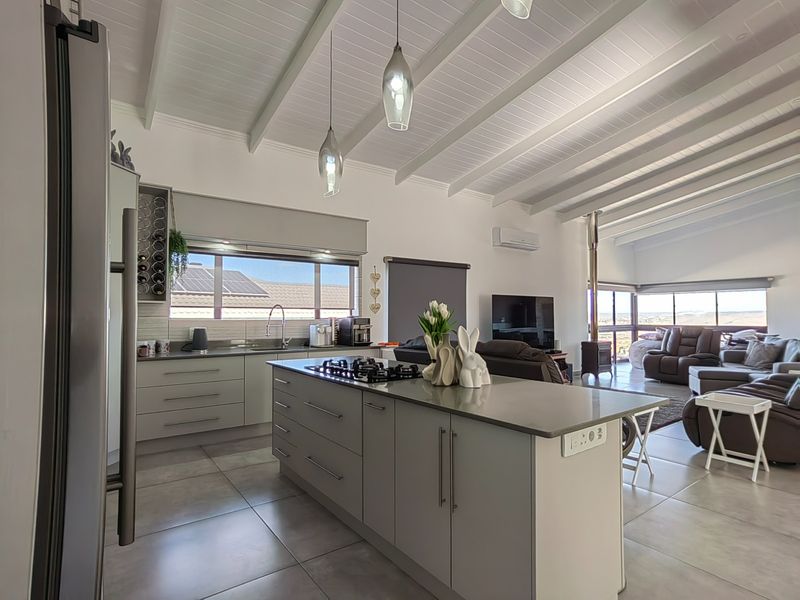 Modern open-plan kitchen and living area featuring a central island with gas hob, exposed beam ceilings, and a cozy wood-burning fireplace.