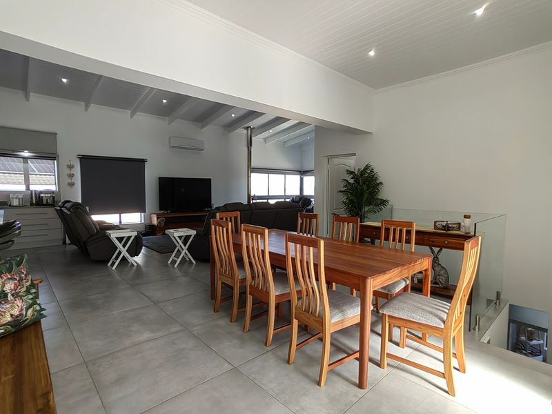 Spacious open-plan living and dining area featuring tiled floors, exposed beam ceilings, recessed lighting, and a modern fireplace, creating a bright and airy atmosphere.