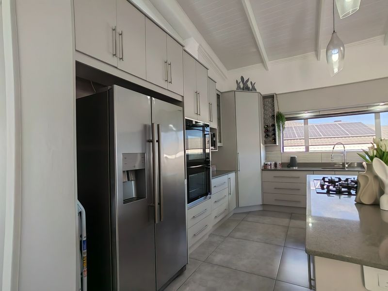 Modern kitchen featuring light grey cabinetry, stone countertops, integrated appliances, gas cooktop, and a vaulted ceiling with tiled flooring.